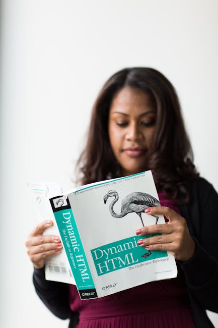 A woman with dark, shoulder-length hair and medium skin tone is holding a thick book titled 'Dynamic HTML' by O'Reilly, featuring a prominent illustration of a crane on the cover. She is wearing a bla